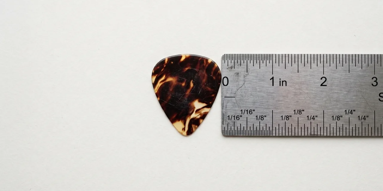 Guitar pick next to a steel ruler, measuring ~1 in (25 mm)
