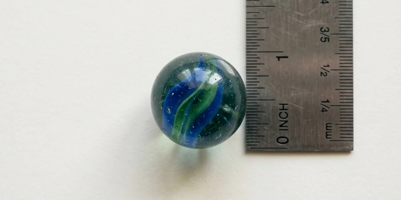 Shooter marble next to a steel ruler, measuring ~1 in (25 mm)